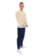Man wearing a beige cardigan, white shirt, and navy pants on a white background