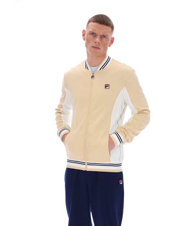 Man wearing a beige and white jacket with navy pants on a white background