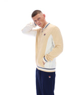 Man wearing a beige and white varsity jacket with navy pants on a white background