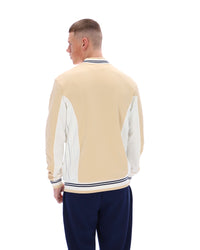 Man wearing a beige and white varsity jacket with navy pants on a white background