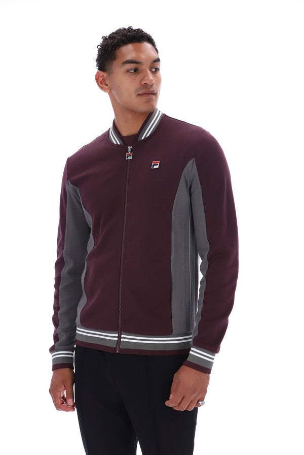 A man wearing a Fila full-zip bomber jacket in maroon and gray with white striped ribbing, photographed against a plain white background.