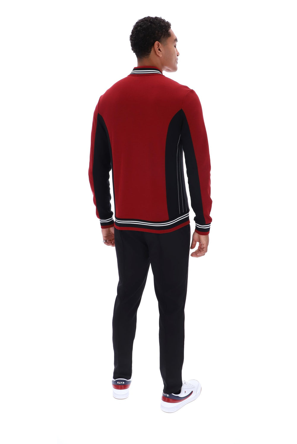 A man shown from the back wearing a red and black knit sweater with white and black striped ribbing, paired with black pants and white sneakers, on a solid white background.