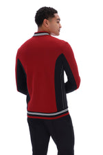 A man shown from the back wearing a red and black color-blocked knit sweater with white striped ribbed trim, paired with black pants, against a solid white background.