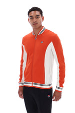 A man wearing a Fila orange and white colorblock zip-up track jacket with black track pants, photographed against a solid white background.