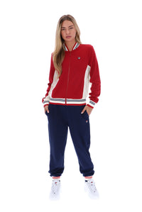 A woman modeling a red, white, and navy blue tracksuit set consisting of a zip-up jacket and matching jogger pants, paired with white sneakers, on a solid white background.