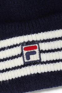 Close-up of a ribbed knit beanie in navy blue and white stripes, featuring a small embroidered Fila logo patch on the front.
