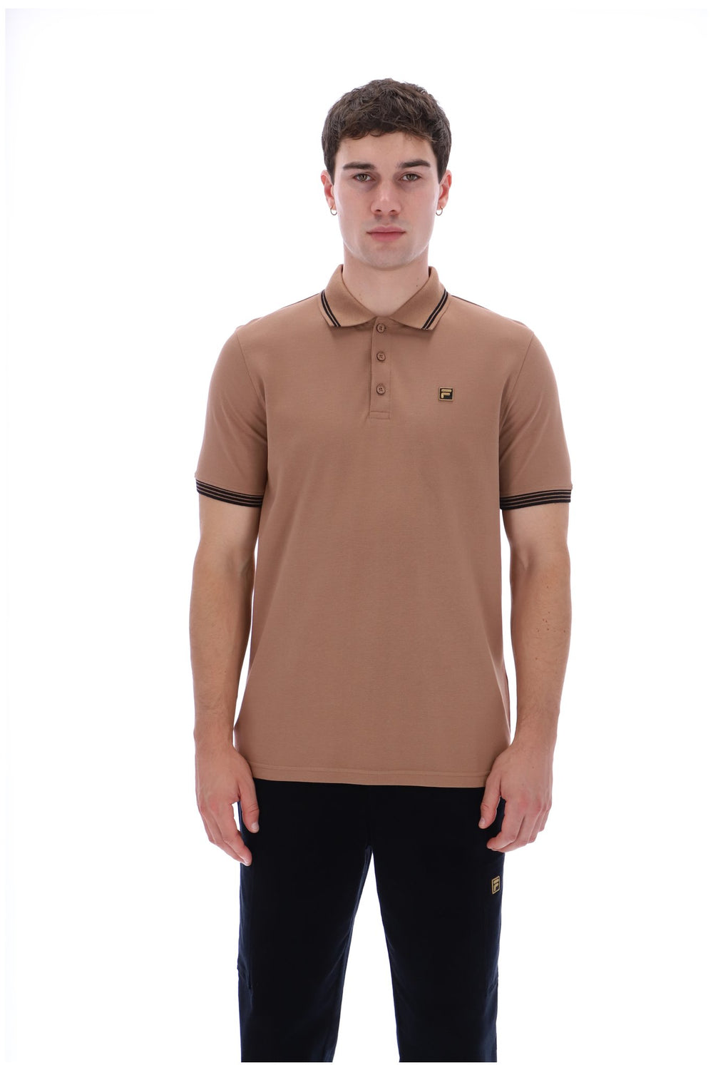 A man modeling a tan short-sleeve polo shirt with dark brown trim on the collar, sleeve cuffs, and a small embroidered logo on the left chest, paired with black pants against a white background.