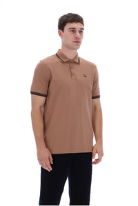 A man modeling a tan short-sleeve polo shirt with black trim on the collar and sleeve cuffs, paired with black pants, against a plain white background.