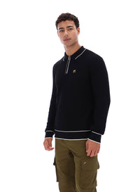 Man wearing a black sweater with white trim and a small FILA Gold logo on the chest, paired with green FILA cargo pants, against a white background