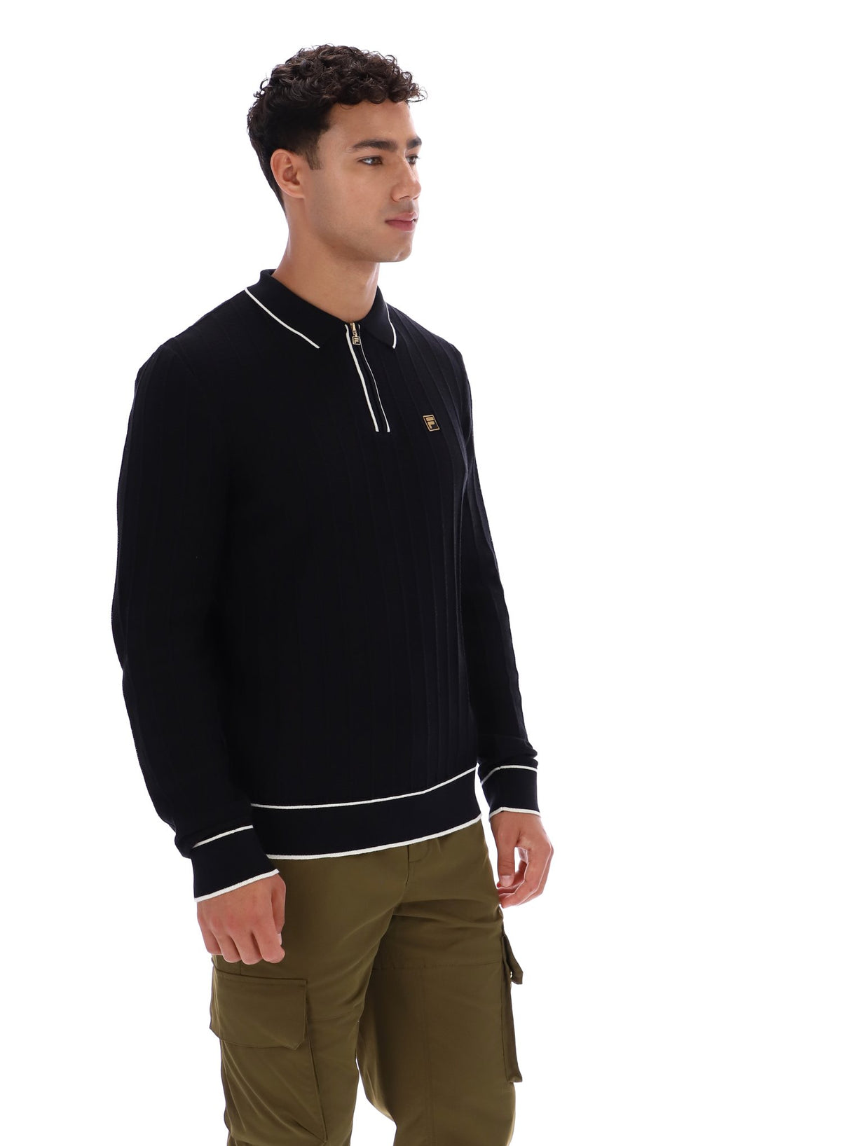 Man wearing a black sweater with white trim and a small FILA Gold logo on the chest, paired with green FILA cargo pants, against a white background