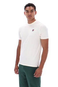A man wearing a white short-sleeve crewneck t-shirt with a small Fila logo on the left chest, paired with dark green pants, against a plain white background.