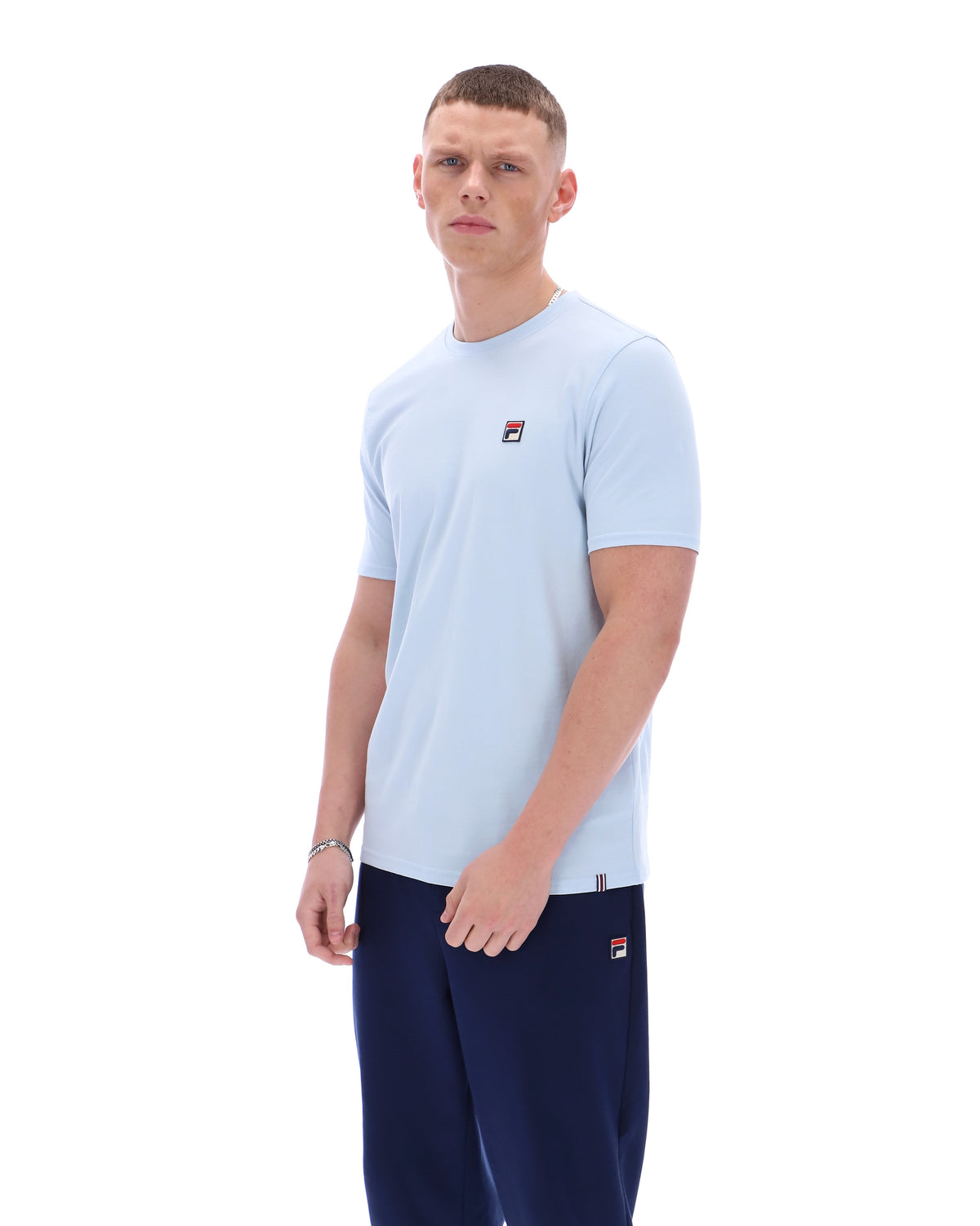 Man wearing a light blue t-shirt and navy pants with a brand logo on a white background