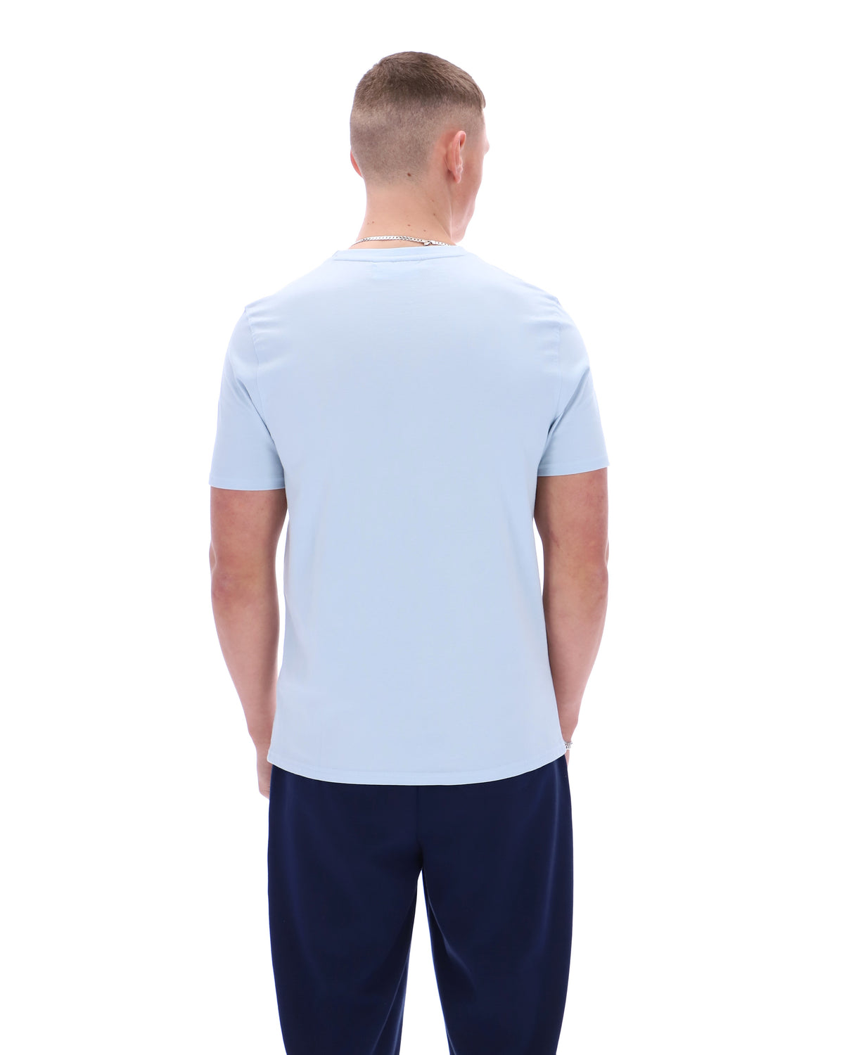 Man wearing a light blue t-shirt and dark blue pants on a white background