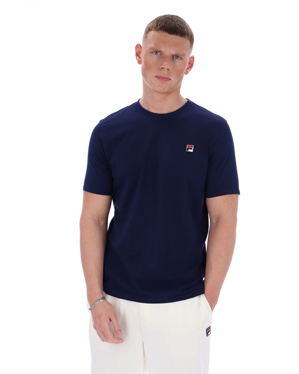 Man wearing a navy blue t-shirt with a small logo on a white background