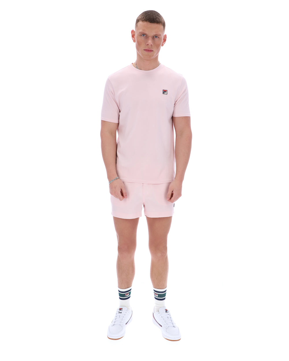 Man wearing a pink t-shirt and shorts set with a visible brand logo on a white background