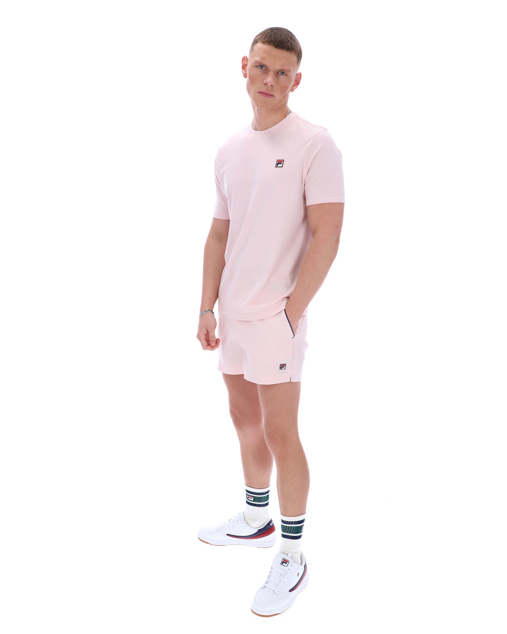 Man wearing a pink t-shirt and shorts set with white sneakers on a white background