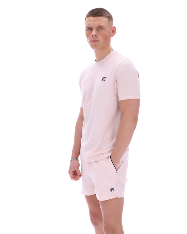 Man wearing a light pink sports outfit with a brand logo on a white background