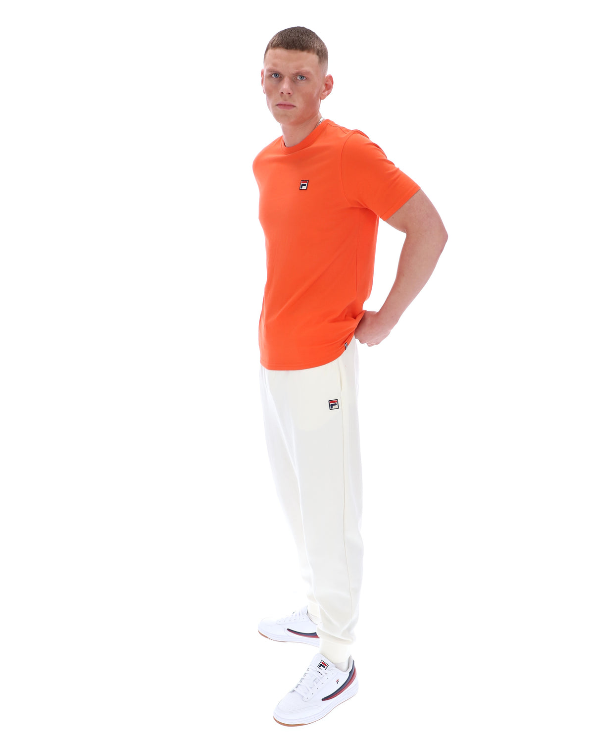 Man wearing an orange t-shirt and white pants on a white background