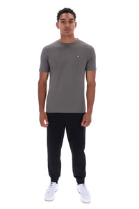 A man modeling a short-sleeve crewneck t-shirt in dark gray, paired with black joggers and white sneakers, against a plain white background.