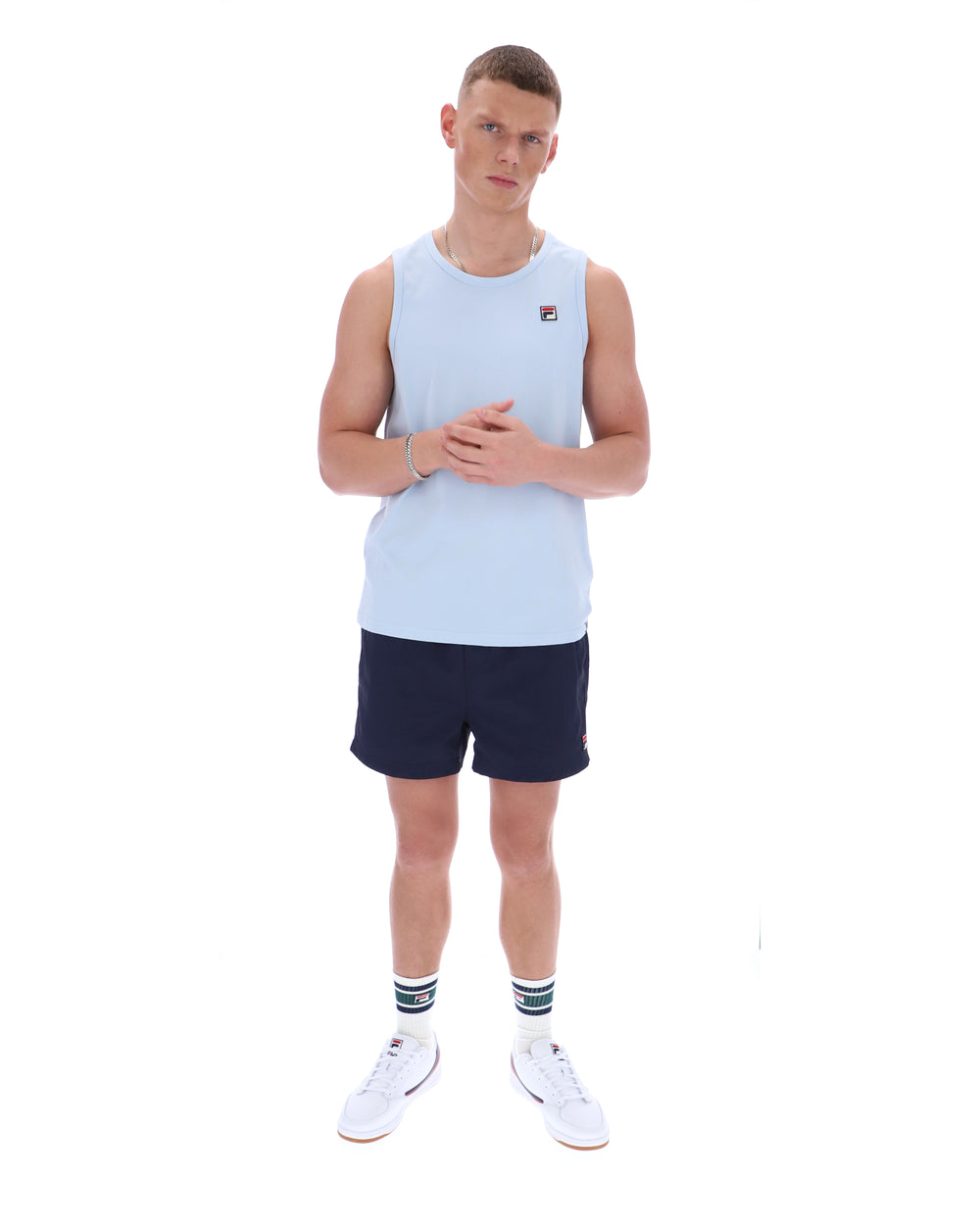 Man wearing a light blue sleeveless shirt and navy shorts on a white background