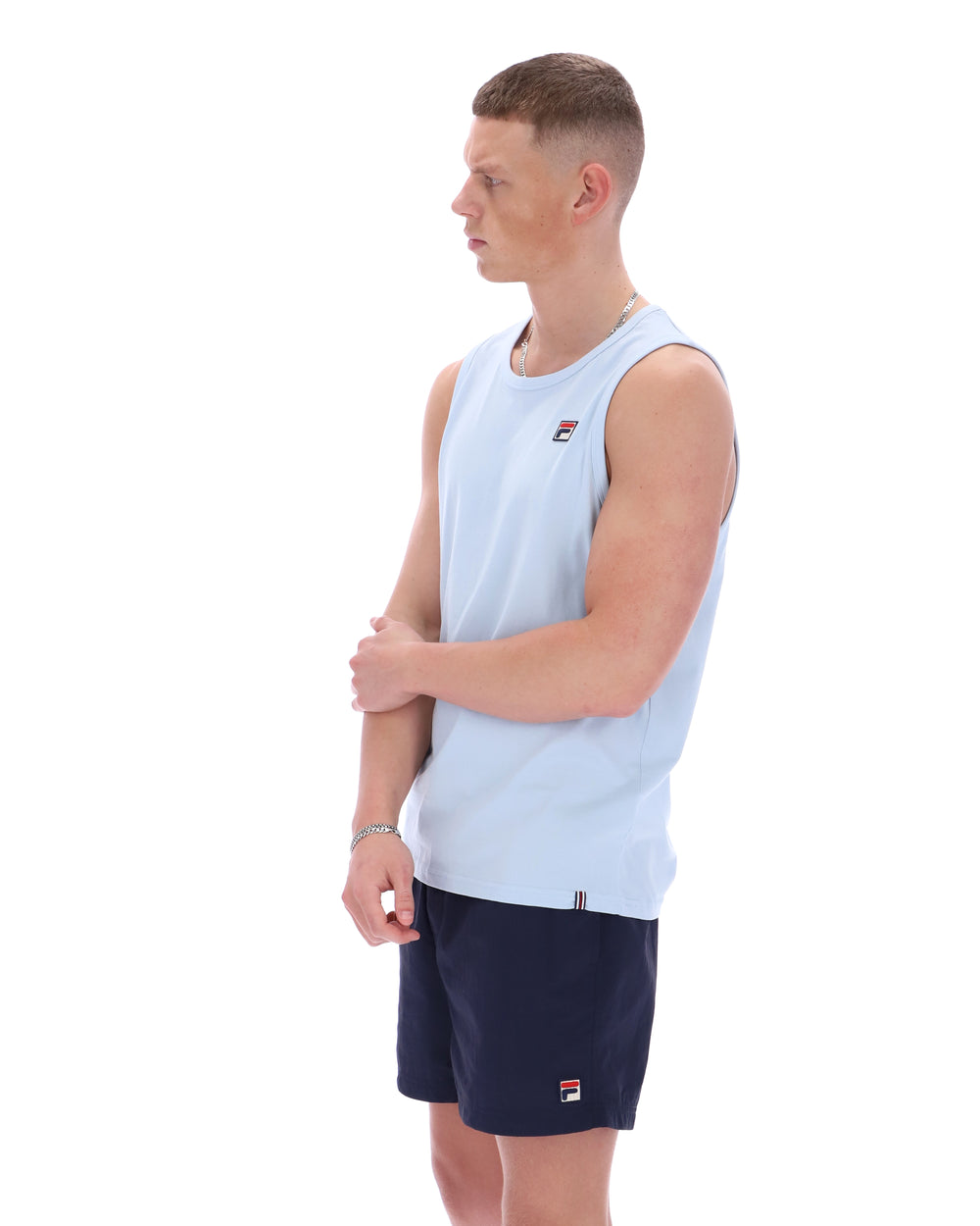 Man wearing a light blue sleeveless shirt and navy shorts with a brand logo on a white background