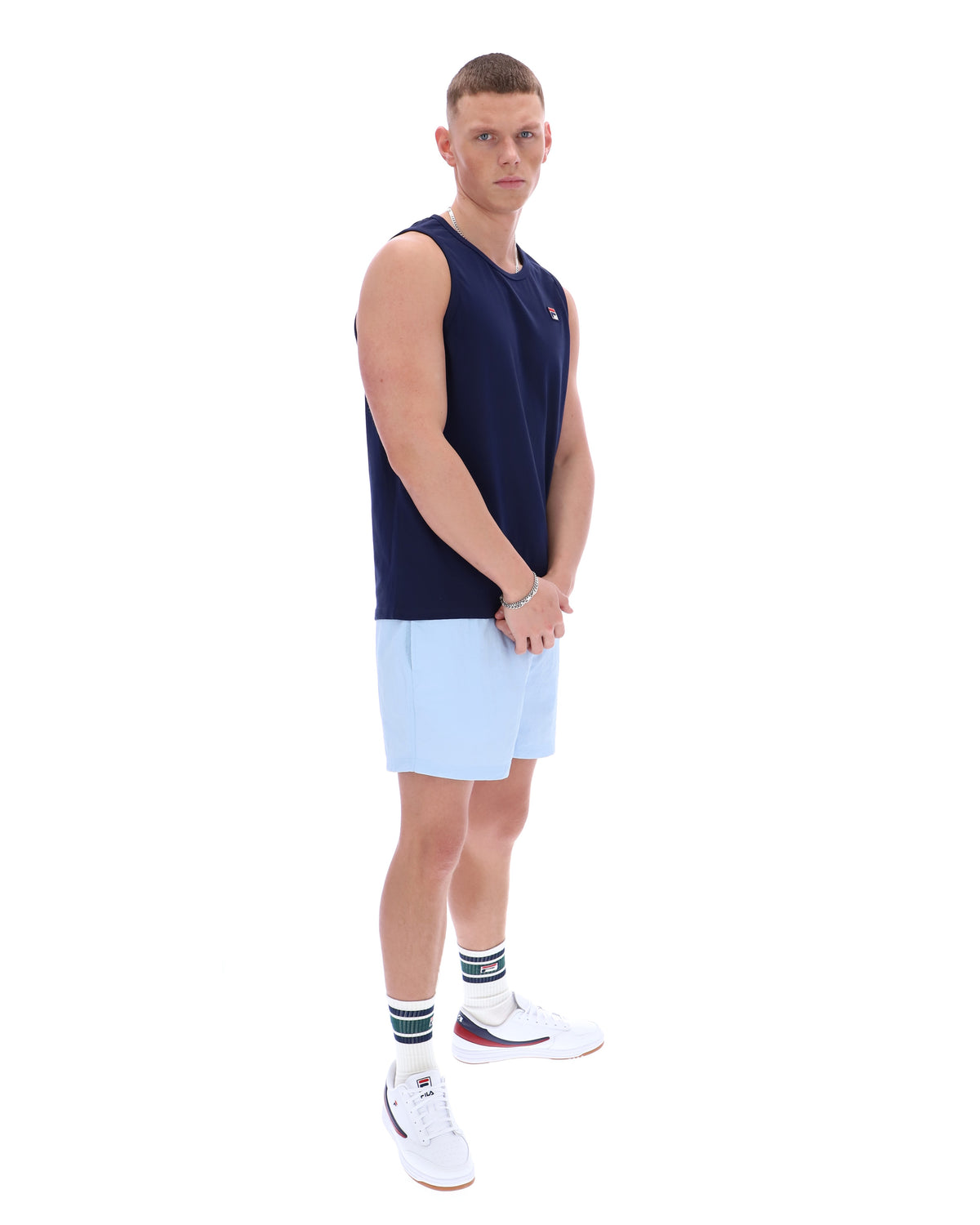 Man wearing a navy sleeveless shirt and light blue shorts on a white background