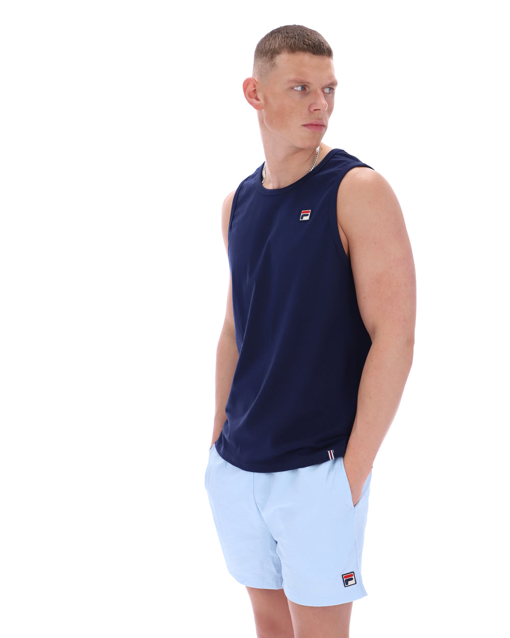 Man wearing a navy sleeveless shirt and light blue shorts on a white background
