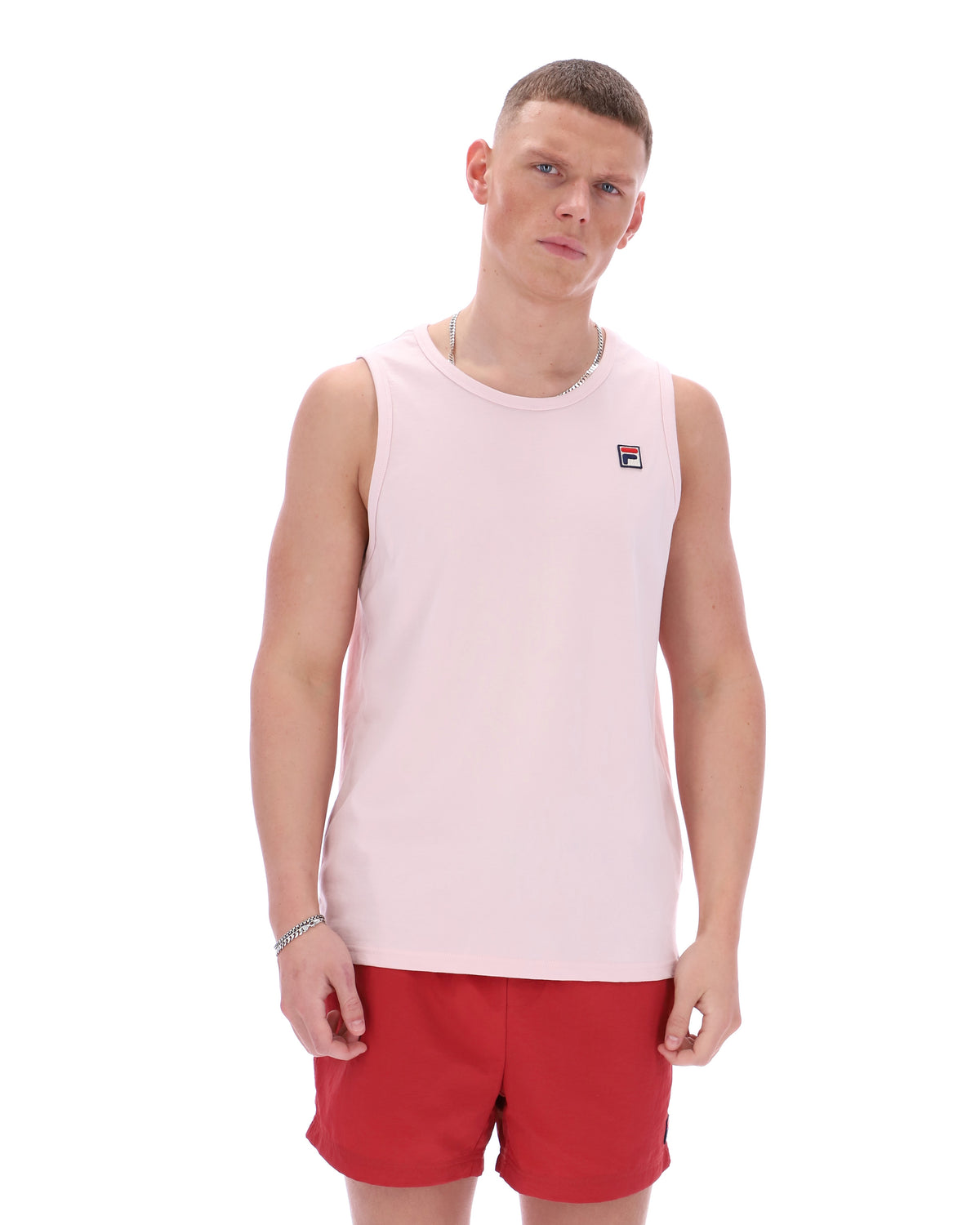 Man wearing a light pink sleeveless shirt with a logo and red shorts on a white background