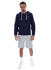 A male model wearing a navy blue zip-up hoodie with the FILA logo on the chest, paired with light grey shorts.