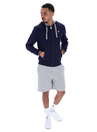 A male model wearing a navy blue zip-up hoodie with the FILA logo on the chest, paired with light grey shorts.