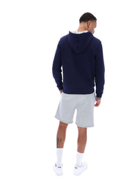 A male model wearing a navy blue zip-up hoodie with the FILA logo on the chest, paired with light grey shorts.