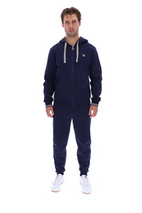 A man modeling a navy blue zip-up hoodie and matching sweatpants set with white drawstrings and white sneakers, photographed against a solid white background.
