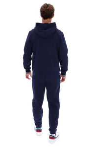 A man viewed from behind wearing a matching navy blue hooded sweatshirt and jogger pants set, paired with white sneakers with red and blue accents, against a plain white background.