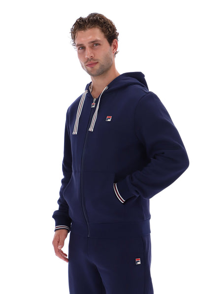 A man wearing a navy blue Fila zip-up hoodie and matching sweatpants, photographed against a solid white background.