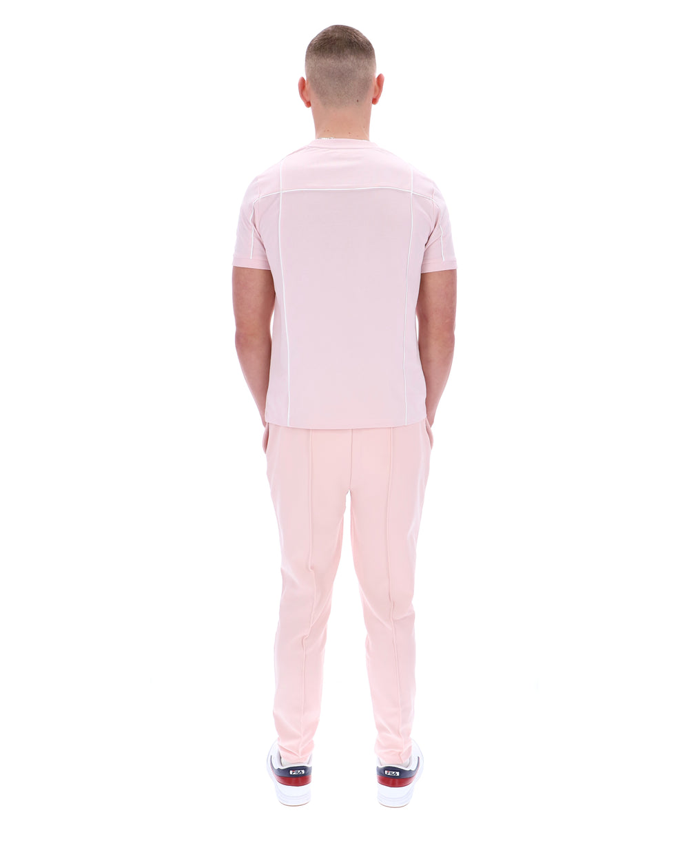 Man wearing a light pink polo shirt and pants on a white background