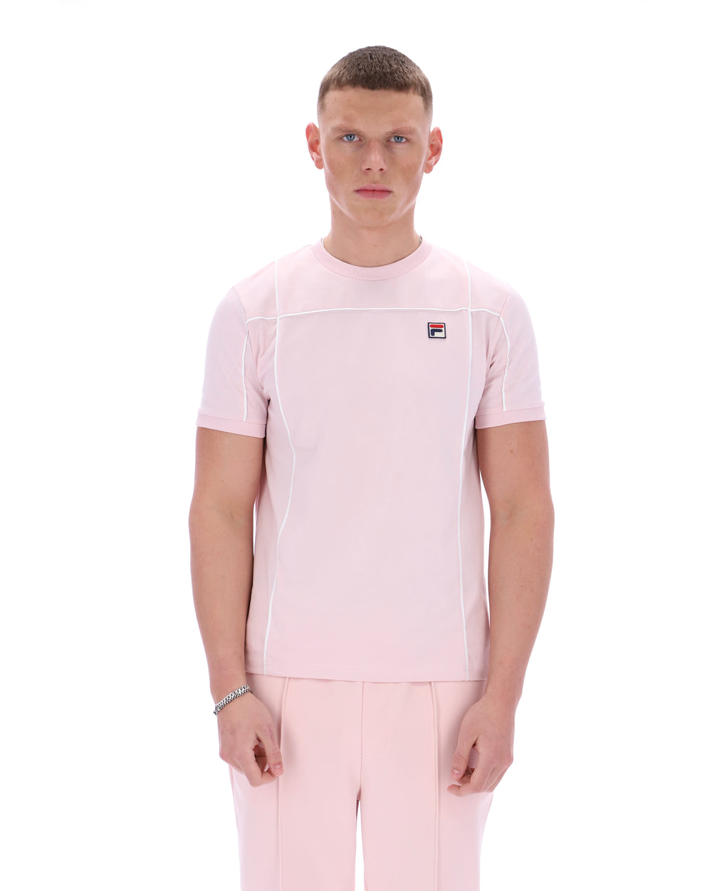 Man wearing a pink t-shirt with a FILA logo on the chest and matching trousers on a white background
