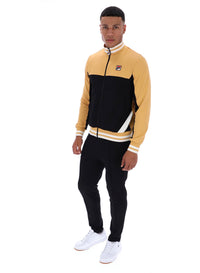 Man wearing a black and beige tracksuit with a FILA logo on the chest, paired with black FILA bottoms, against a white background