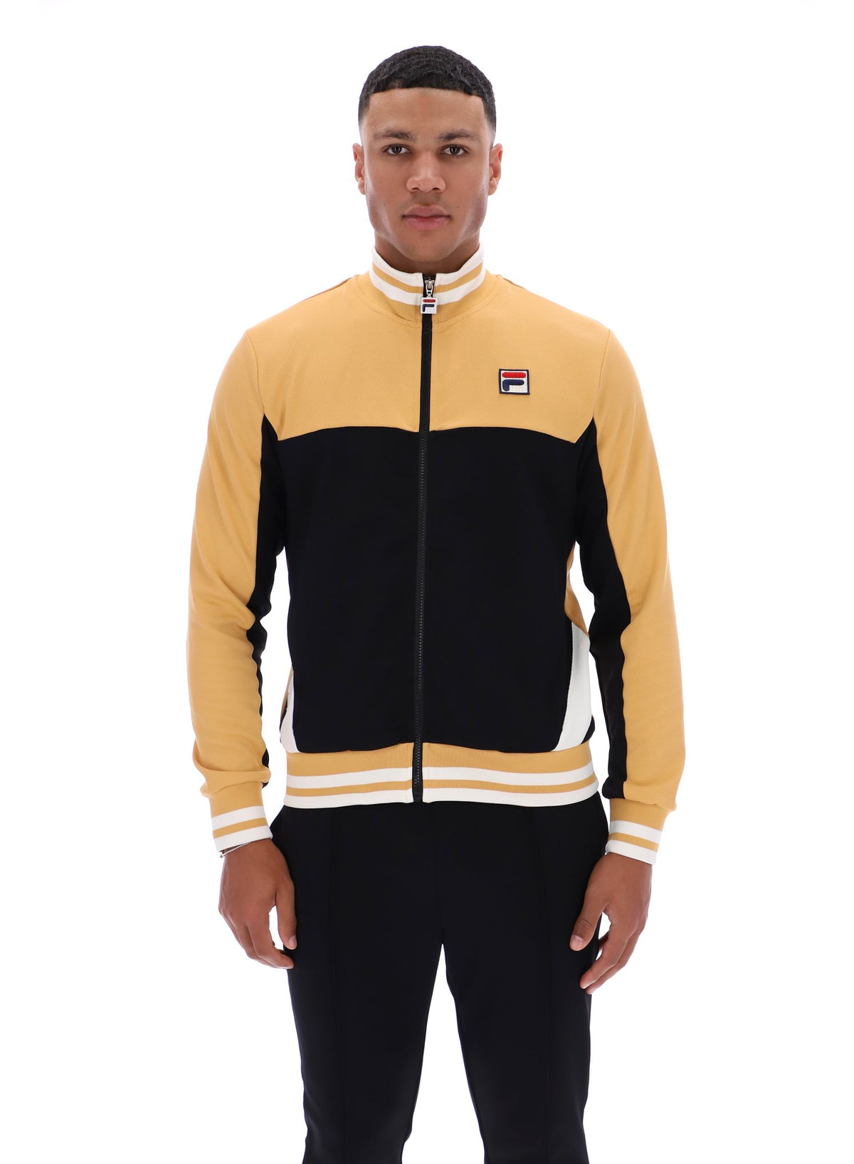 Man wearing a black and beige tracksuit with a FILA logo on the chest, paired with black FILA bottoms, against a white background