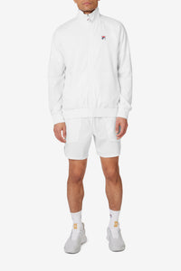 A man wearing a white FILA tennis court track jacket with a zipper, collar, and matching white shorts.