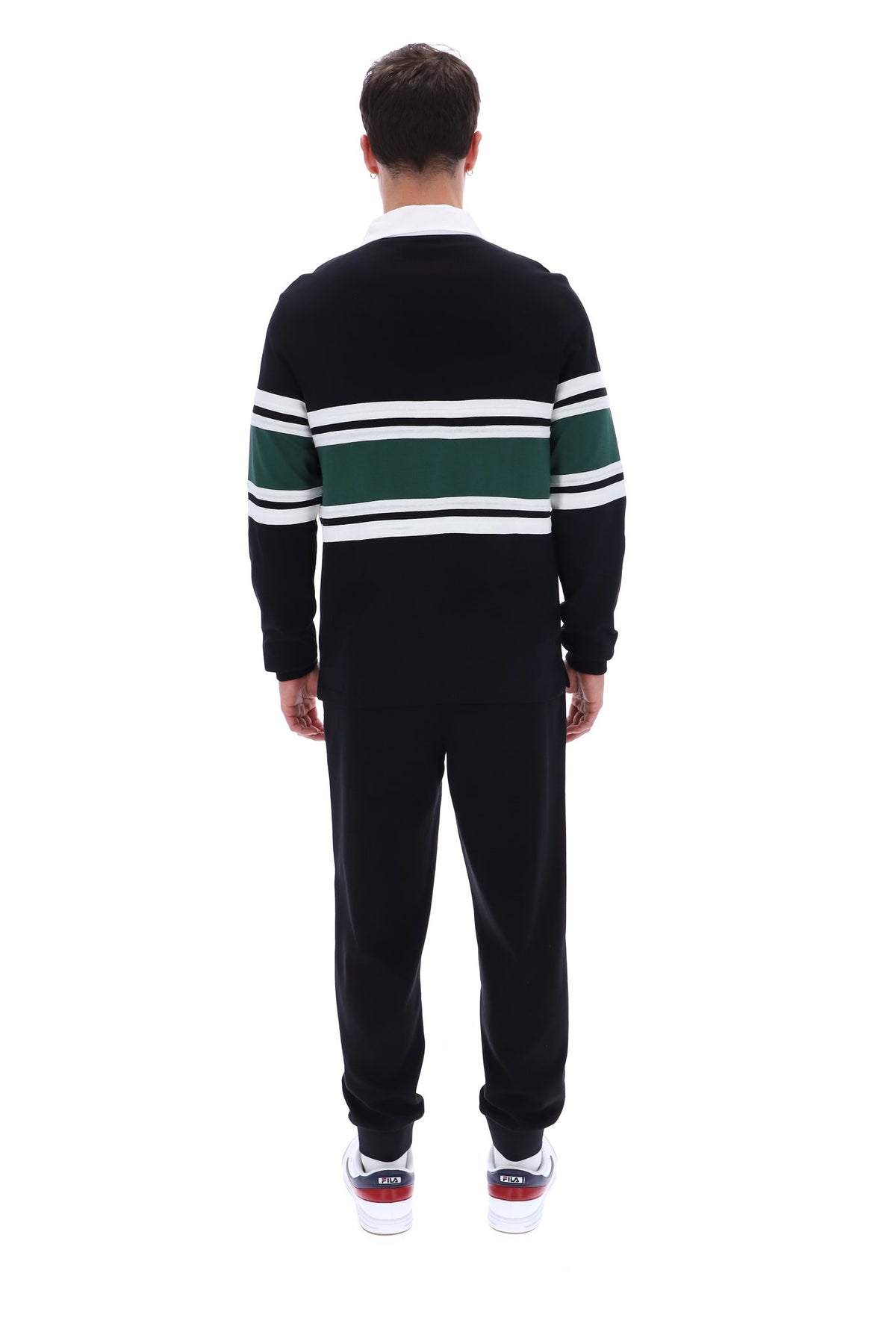 A man viewed from behind wearing a black knit sweater with green and white horizontal stripes across the shoulders and upper arms, paired with black sweatpants and white sneakers.