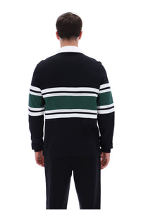 A man viewed from the back wearing a dark navy long-sleeve knit sweater with horizontal green and white stripes across the chest and sleeves, paired with dark trousers, on a plain white background.