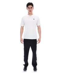 Man wearing a white t-shirt with a small FILA gold logo, paired with black pants, against a white background