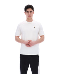 Man wearing a white t-shirt with a small FILA gold logo on a white background