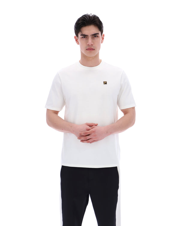 Man wearing a white t-shirt with a small FILA gold logo on a white background