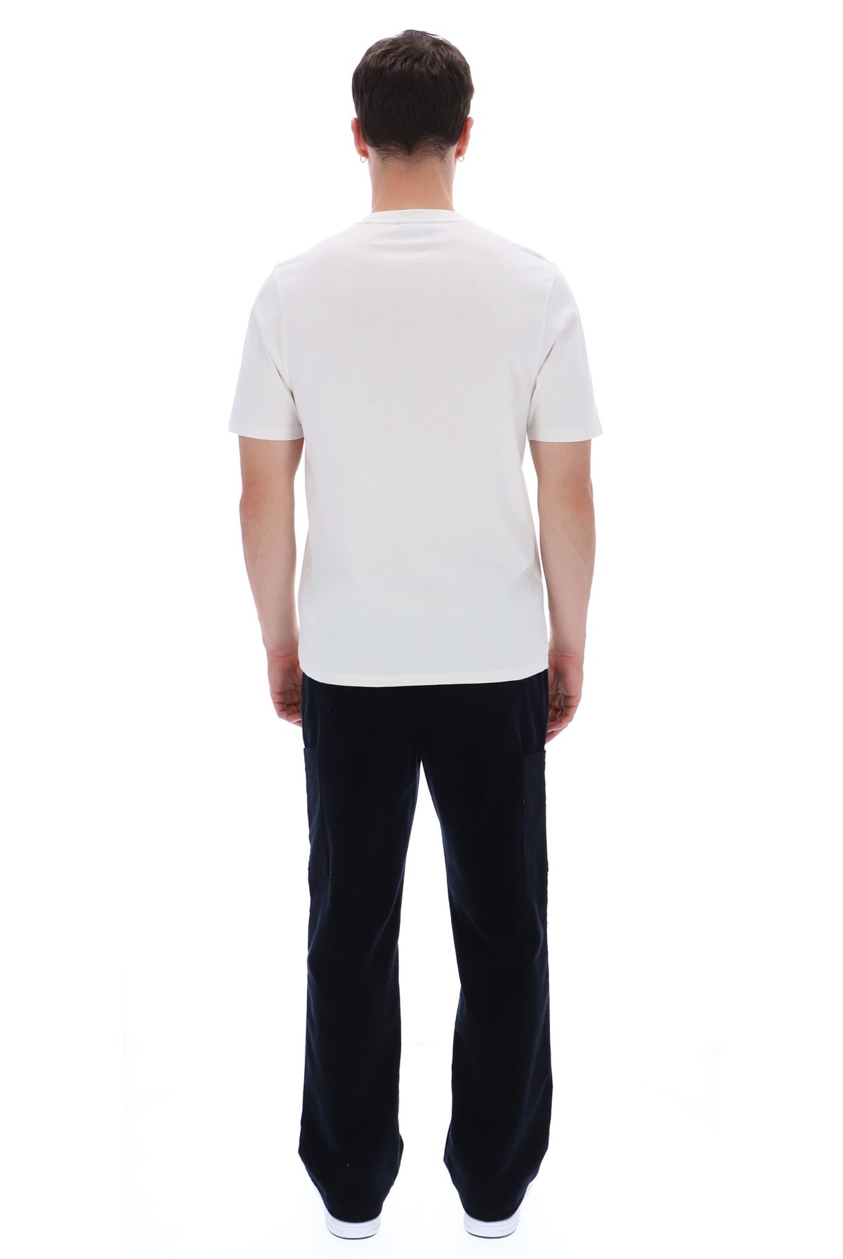 A man viewed from behind wearing a plain white short-sleeve t-shirt and dark navy pants, standing against a solid white background.