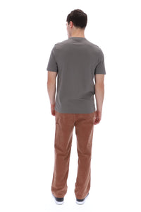 A man viewed from behind wearing a dark gray short-sleeve t-shirt and brown corduroy pants, standing against a solid white background.