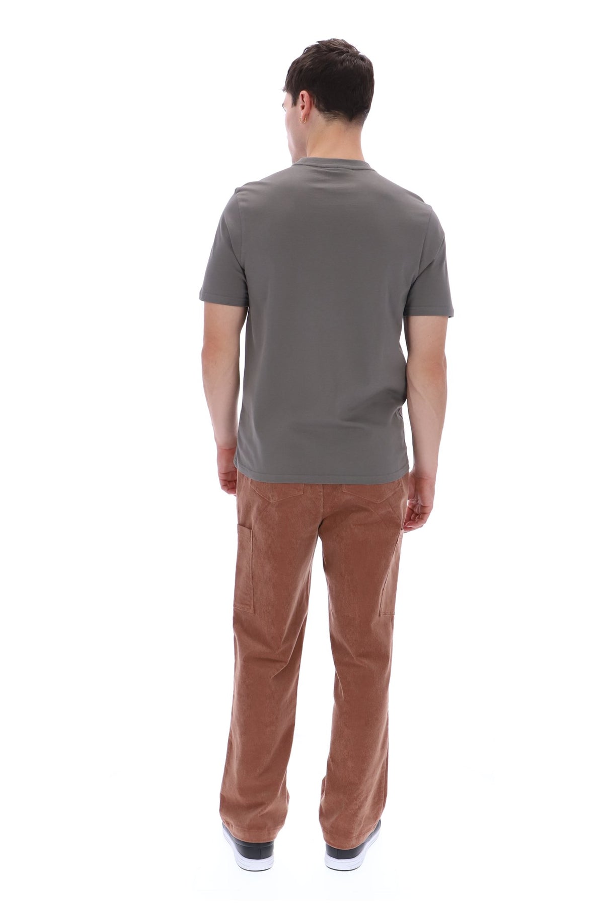 A man viewed from behind wearing a dark gray short-sleeve t-shirt and brown corduroy pants, standing against a solid white background.