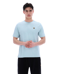 Man wearing a light blue t-shirt with a small logo on a white background