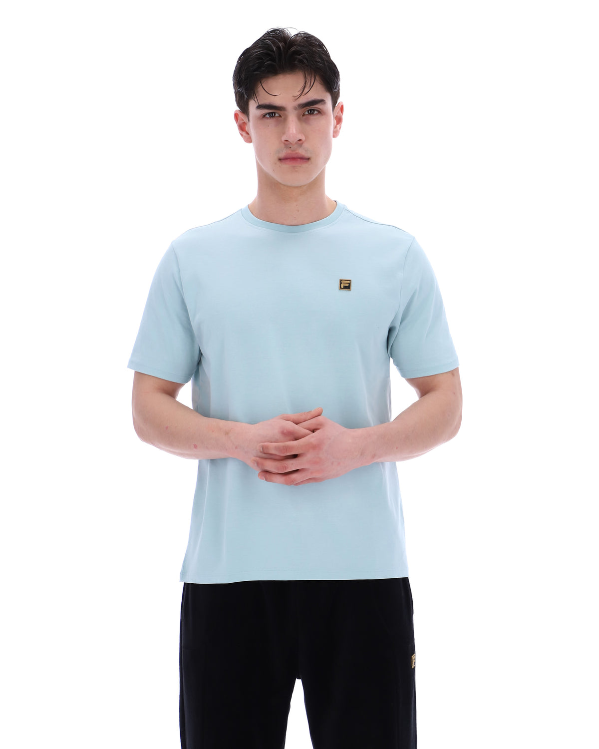 Man wearing a light blue t-shirt with a small logo on a white background