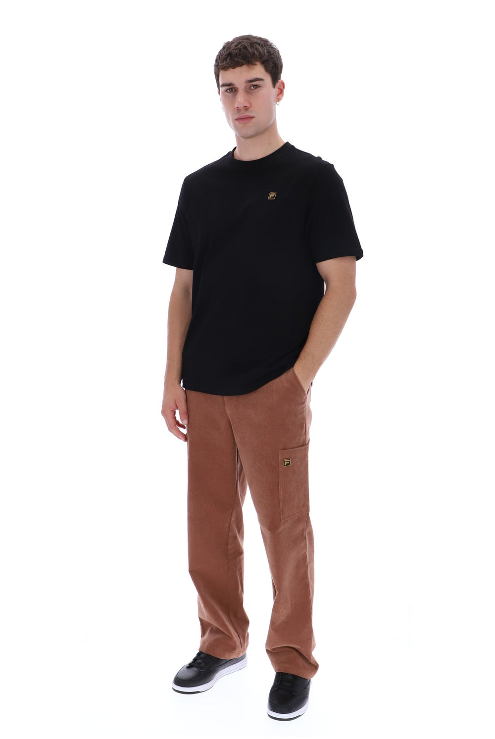 A man modeling a black crewneck t-shirt and brown corduroy cargo pants against a solid white background.